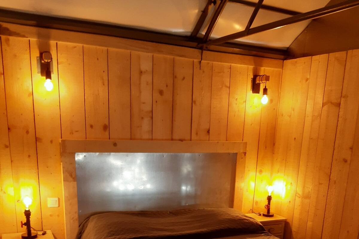 A wooden-paneled room with a bed, two bedside tables with lamps, and a metal headboard.