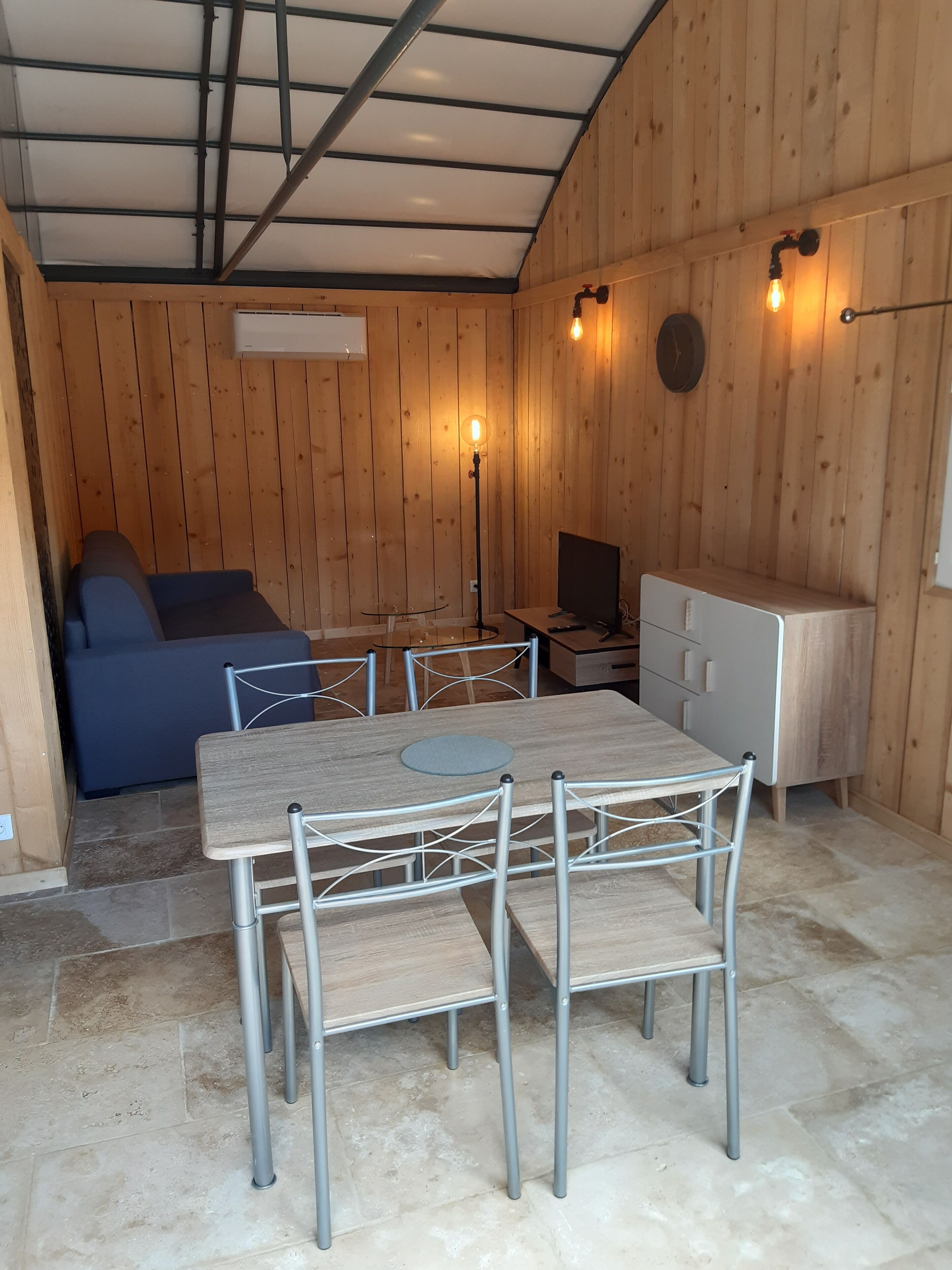 Une pièce de taille modeste, avec un intérieur en bois, une table à manger avec des chaises, un canapé, une petite télévision et une lampe.