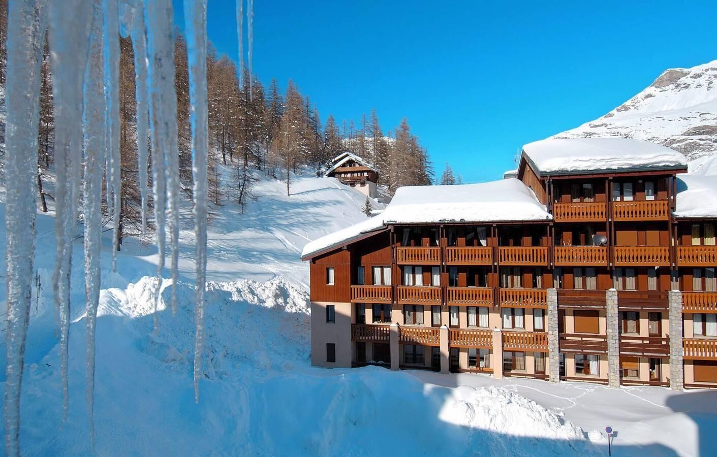 A multi-story hotel with balconies and a snow-covered roof, surrounded by a snowy landscape and trees.