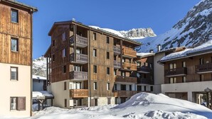 A multi-story wooden building with balconies, set against a snowy mountain backdrop.