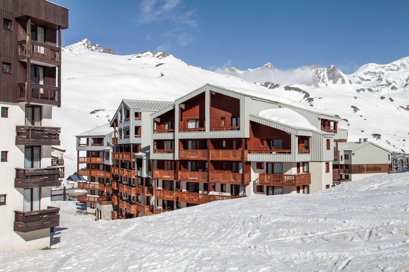A multi-story hotel with balconies, set against a snowy mountain backdrop.