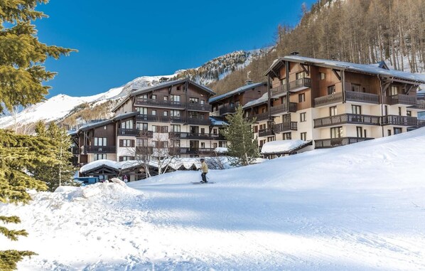 A ski resort with multiple wooden buildings, ski slopes, and snow-covered mountains. - 300m from ski slopes, terrace, balcony, tv, ski locker, 26-28m², Val d'Isère (Val-d'Isère)