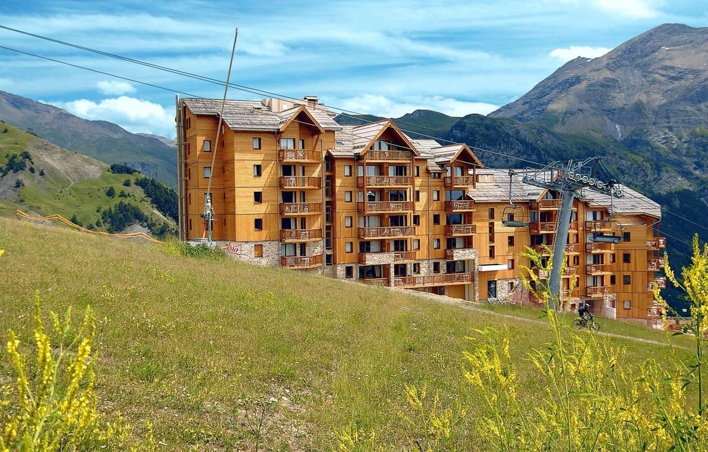 A multi-story wooden building with balconies, set against a mountainous backdrop.