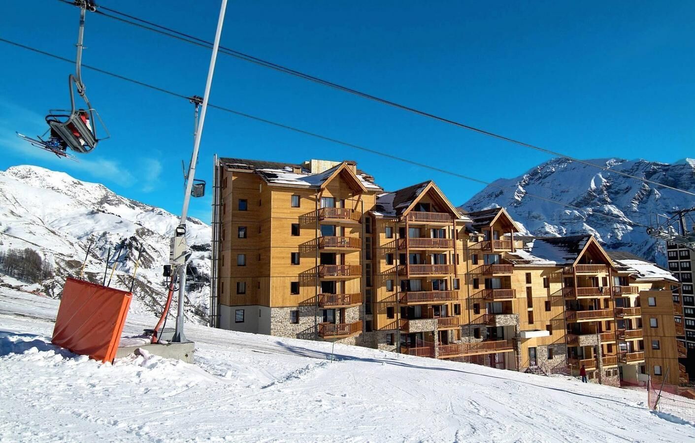 Ein mehrstöckiges Holzhaus mit Balkonen vor einer verschneiten Bergkulisse.