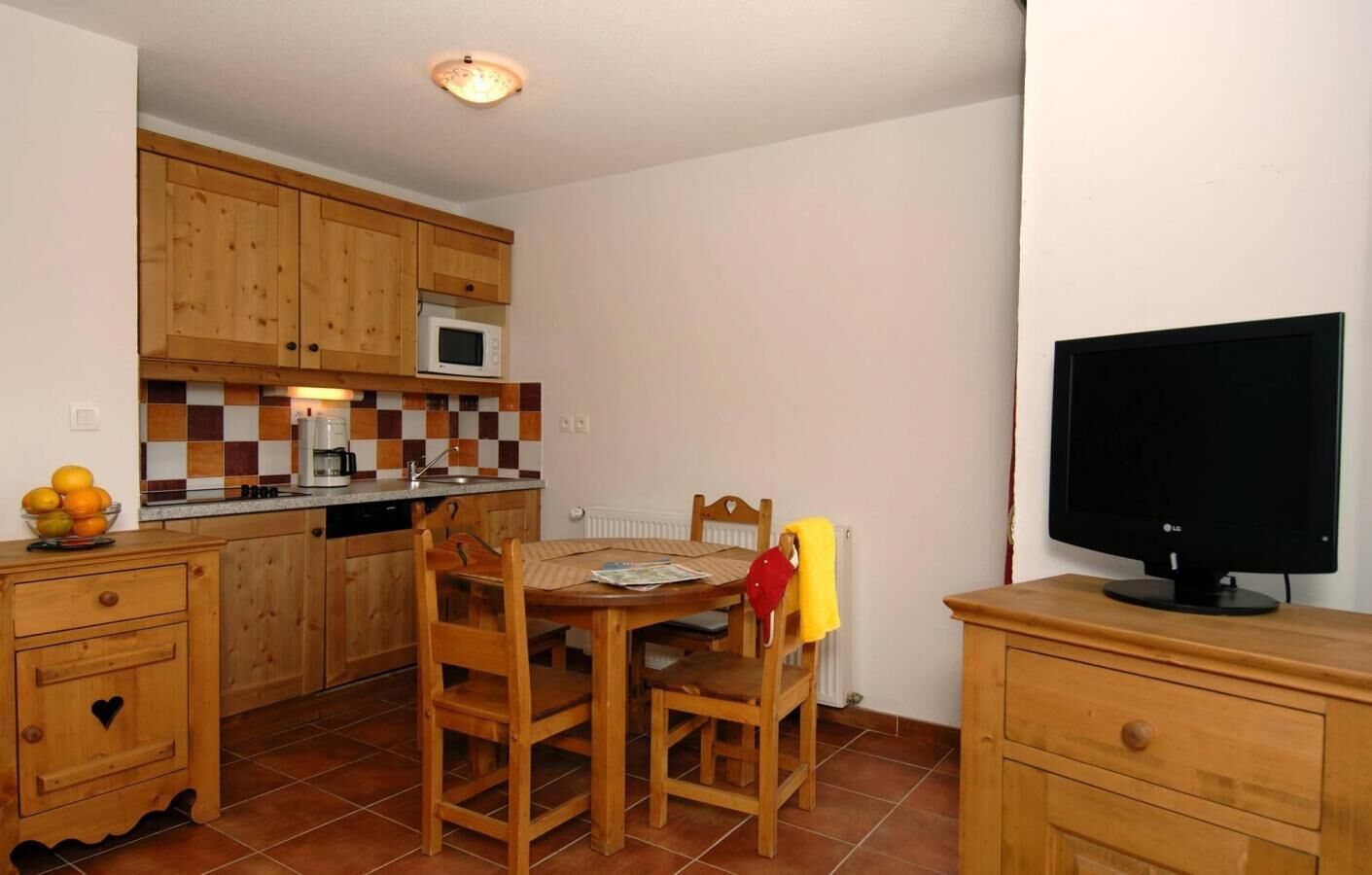 A compact kitchen with wooden cabinets, a microwave, and a dining table with chairs.