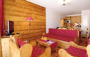 A cozy wooden interior with a sofa, chairs, a small table, a television, and a kitchen area.