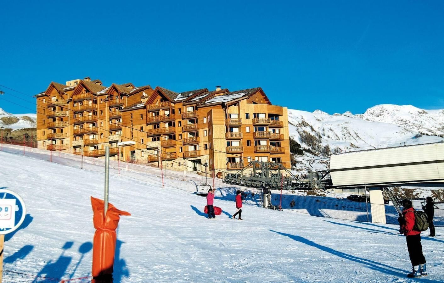 A multi-story wooden building with balconies, likely a hotel or resort, with a ski slope in the foreground.