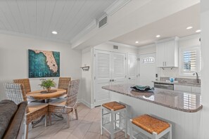 A modern kitchen with white cabinetry, a granite countertop, and a dining area with wicker chairs and a round table.