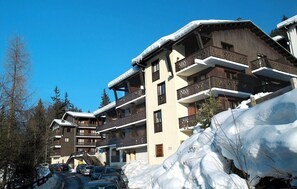 Un edificio de varios pisos con balcones, rodeado de nieve y árboles.
