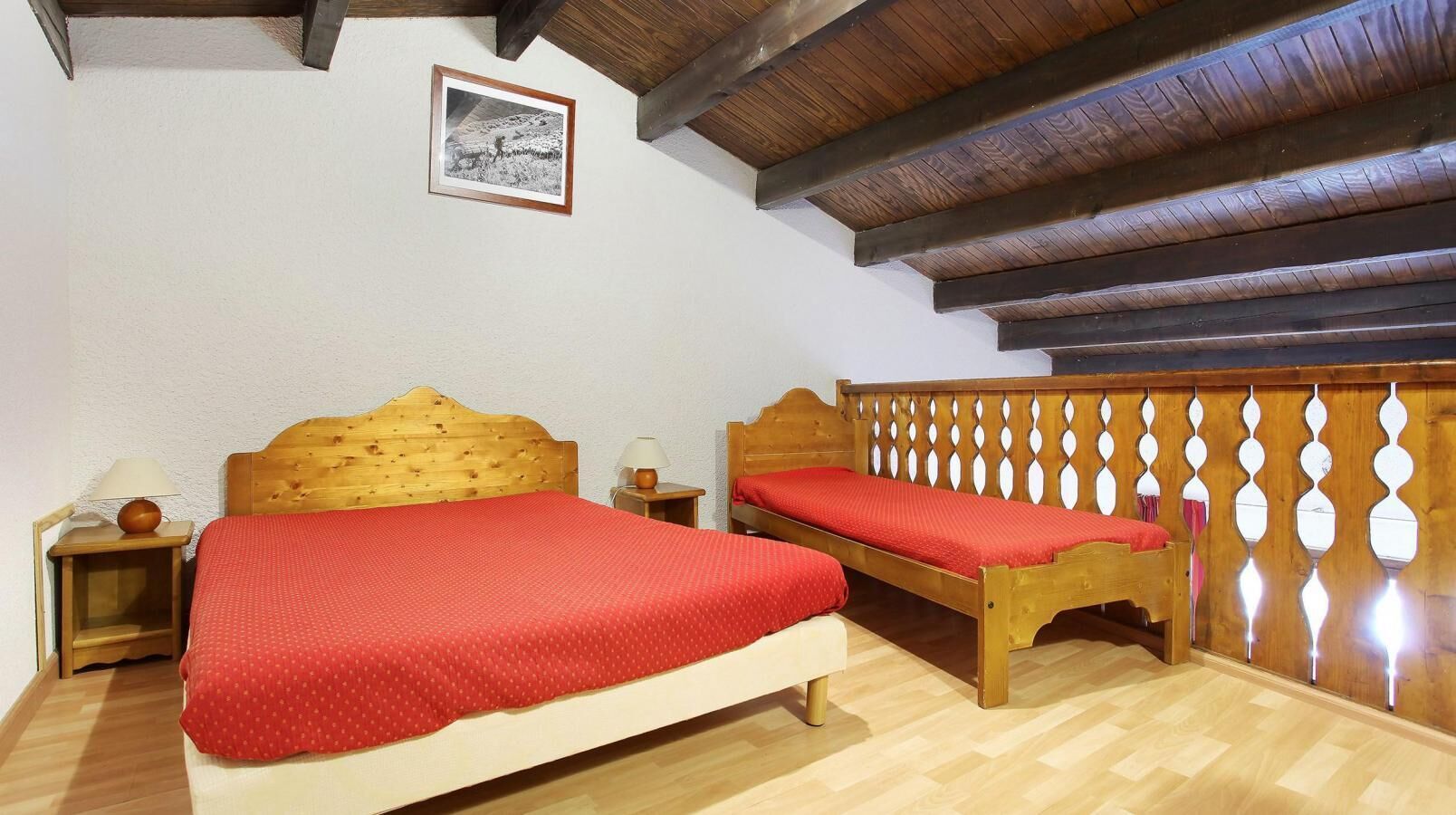 Une chambre à coucher avec deux lits en bois, une tête de lit en bois, une petite table de chevet avec une lampe et un tableau encadré accroché au mur.