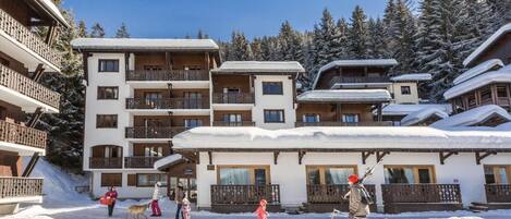 A multi-story hotel with balconies and a ski slope in the background.