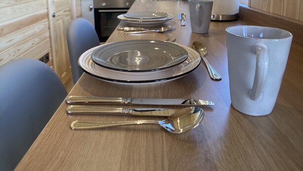 A wooden interior with a dining table set for two, equipped with plates, cutlery, and a mug. - The Cedar Tiny House (Coldingham)
