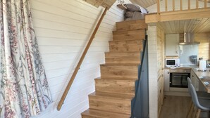 A wooden staircase leading to a kitchen with a microwave and a sink. - The Cedar Tiny House (Coldingham)