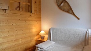 A wooden cabin room with a bed, a nightstand with a lamp, and a wall-mounted paddleboard. - 300m from shops, 2nd floor, balcony, ski locker, 40m², Méribel (Méribel - Les Allues)