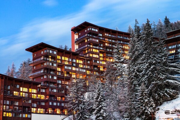 Un hotel de varios pisos con balcones e iluminación cálida, rodeado de árboles cubiertos de nieve.