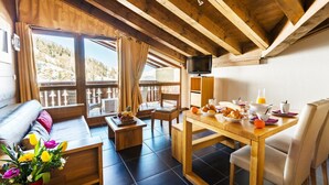 Een gezellige kamer met houten plafond, een balkon met uitzicht, een ontbijt gedekte eettafel, en een televisie aan de muur.