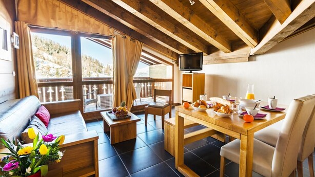 A cozy room with a wooden ceiling, a balcony with a view, a dining table set with breakfast, and a TV on the wall. - 30m from ski slopes, swimming pool, tv, ski locker, 51m², La Plagne (La Plagne)