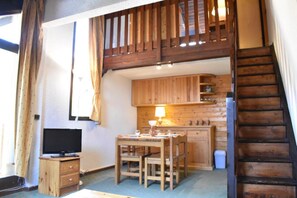 A compact kitchen with wooden cabinets, a dining table with chairs, a television on a wooden stand, and a staircase leading to an upper level. - 200m from ski slopes, 5th floor, terrace, tv, ski locker, 30m², Méribel (Méribel - Les Allues)