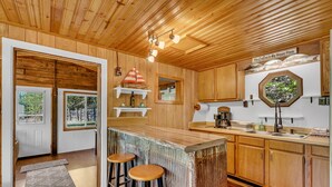 Cocina de cabaña de madera con barra, armarios de madera y ventana con vistas a vegetación.