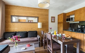 Una sala de estar acogedora con una pared de madera, un sofá, una mesa de comedor con sillas y una zona de cocina con armarios y electrodomésticos de madera.