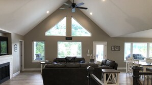 A spacious living room with a high ceiling, large windows, a fireplace, and a dining area with a table and chairs.