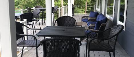 A covered outdoor patio with a table and chairs, surrounded by windows.