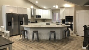 A modern kitchen with stainless steel appliances, a central island with stools, and pendant lighting.