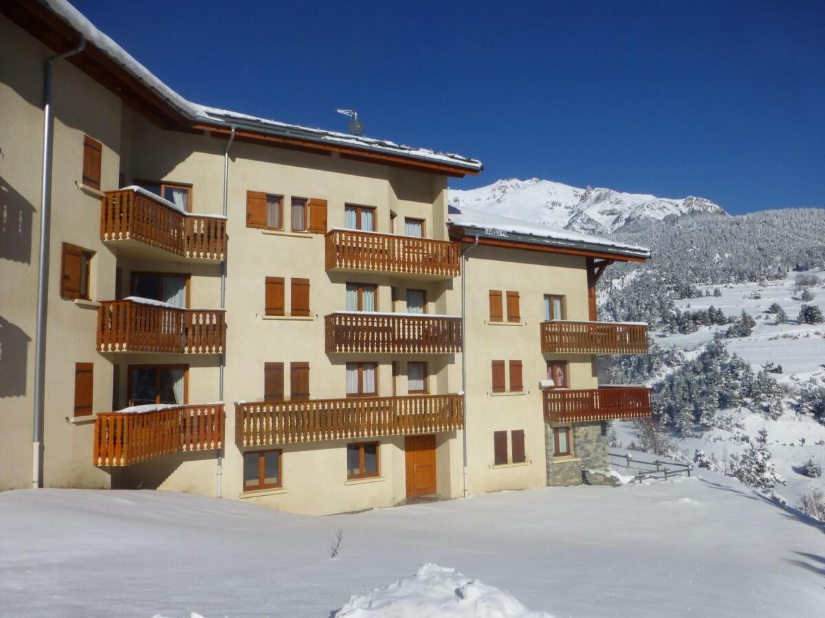 A multi-story building with balconies, set against a snowy mountain backdrop.