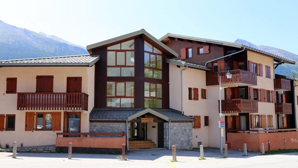 Un hôtel à plusieurs étages, doté d’une façade en pierre, de balcons en bois et surplombant un paysage montagneux.