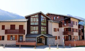 A multi-story hotel with a stone facade, wooden balconies, and a mountain backdrop. - Terrace, tv, ski locker, 25m², Aussois (Aussois)