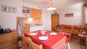 Une cuisine compacte avec des meubles en bois, une table à manger pour deux personnes et un canapé dans l’espace salon.