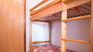 Une chambre avec un lit superposé, une porte en bois et un sol carrelé.