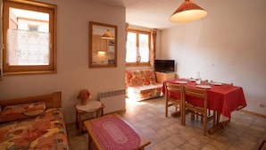Un salon confortable avec un canapé, une petite table, une table à manger avec des chaises, un téléviseur et une fenêtre avec des rideaux.
