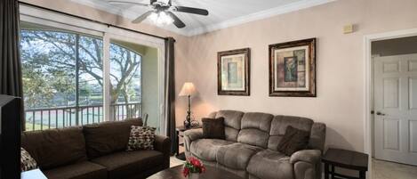 A living room with a ceiling fan, a sofa, a coffee table with flowers, and framed pictures on the wall.