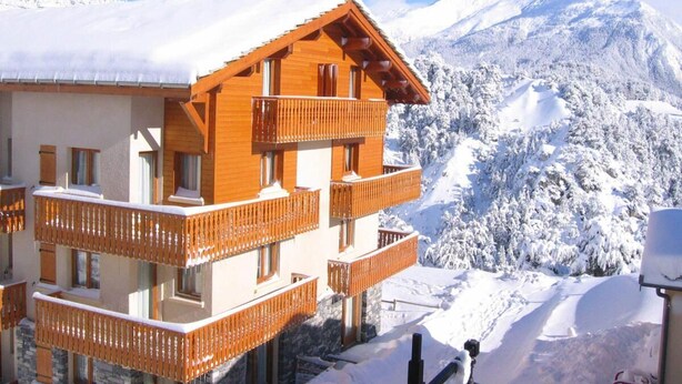 A multi-story wooden building with balconies, set against a snowy mountain backdrop. - 1st floor, balcony, tv, ski locker, 40m², Aussois (Aussois)