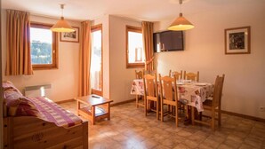 A cozy room with a bed, a small table, a dining table with chairs, a TV on the wall, and a window with curtains. - 1st floor, balcony, tv, ski locker, 40m², Aussois (Aussois)