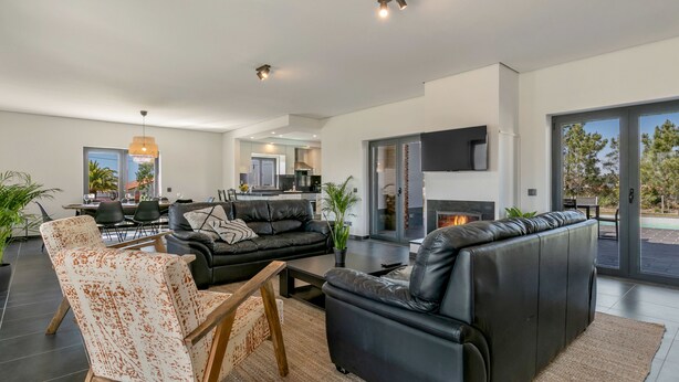Een moderne woonkamer met een zwarte leren bank, een rustieke fauteuil en een open haard.