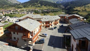 Un village de montagne aux bâtiments traditionnels en bois, doté d’un parking central et offrant une vue sur les collines environnantes.