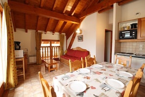 A cozy dining area with a wooden table set for four, a red sofa, and a kitchen with a microwave. - 1st floor, balcony, tv, ski locker, 41m², Aussois (Aussois)