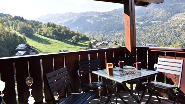 En træterrasse med bord og stole med udsigt over et bjerglandskab.