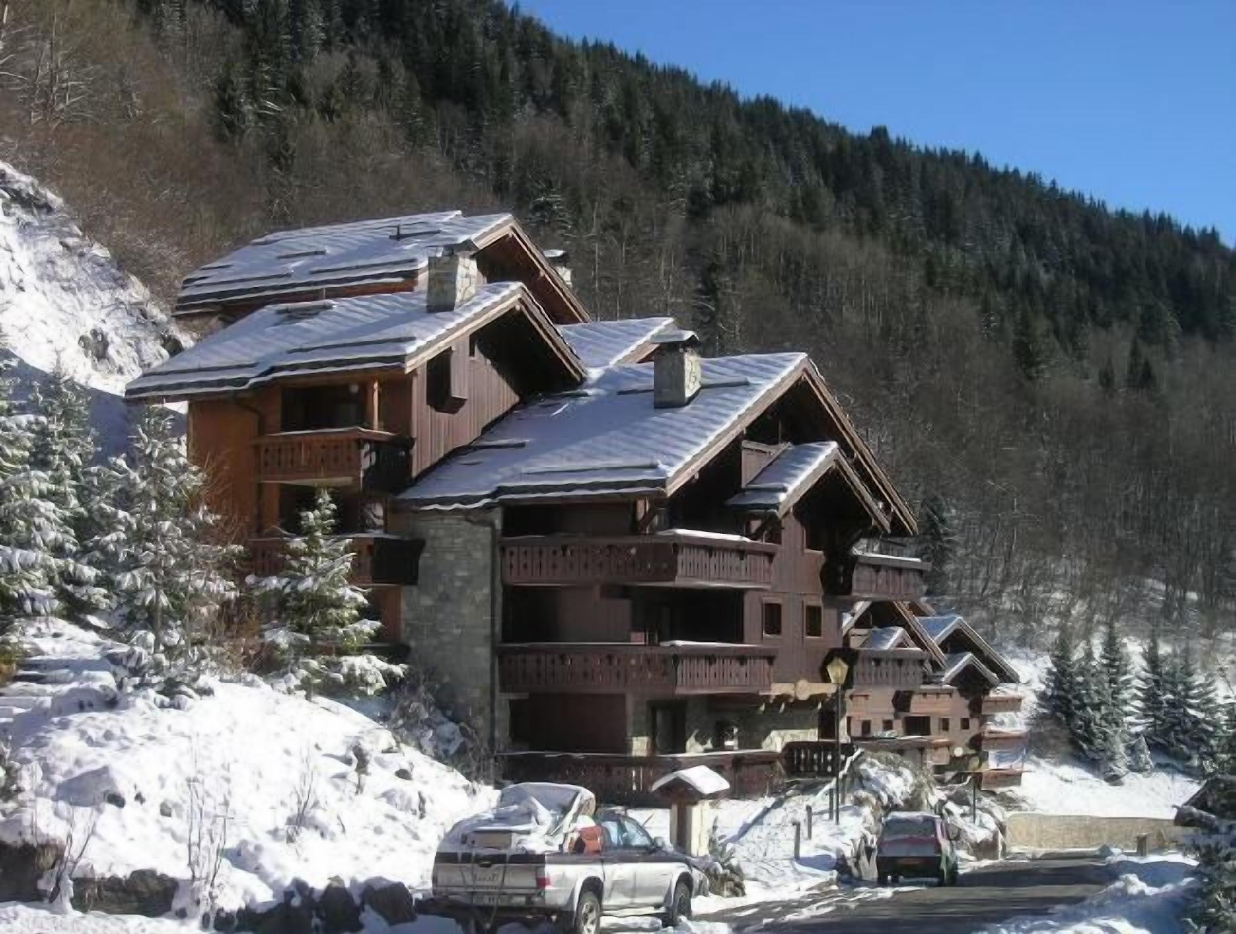 Ein mehrstöckiges Holzgebäude mit Balkonen, umgeben von schneebedeckten Bäumen und einer Bergkulisse.