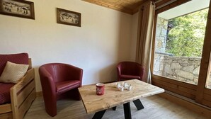 Et værelse med et træbord, to røde stole, en træsofa og et vindue med udsigt til en stenvæg.