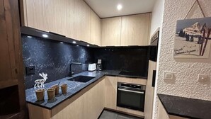 Una cocina compacta con armarios de madera, una encimera negra y un horno empotrado.