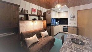 Un espacio habitable compacto con sofá, mesa de comedor, kitchenette y techo de madera.