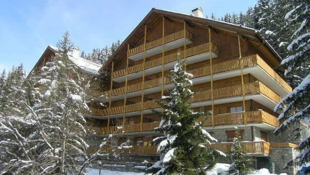 Un edificio de madera de varios pisos con balcones, rodeado de árboles cubiertos de nieve.