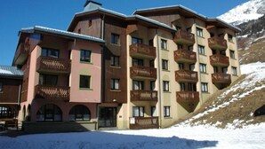 Een hotel met meerdere verdiepingen en balkons, met een skipiste op de achtergrond en een besneeuwde grond.