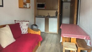 A compact room with a red sofa, a small wooden table with a checkered tablecloth, and a kitchenette area with a microwave and a refrigerator. - 200m from resort center, 4th floor, balcony, 28m², Val Thorens (Val Thorens)