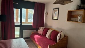 A cozy room with a wooden sofa, a small wooden table, a window with curtains, and a hanging light fixture. - 200m from resort center, 4th floor, balcony, 28m², Val Thorens (Val Thorens)