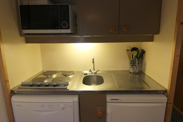 Een kleine keuken met een magnetron, fornuis, spoelbak en vaatwasser.