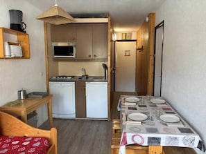 Cocina funcional con microondas, estufa y refrigerador. Se aprecia una mesa de comedor con platos y vasos.